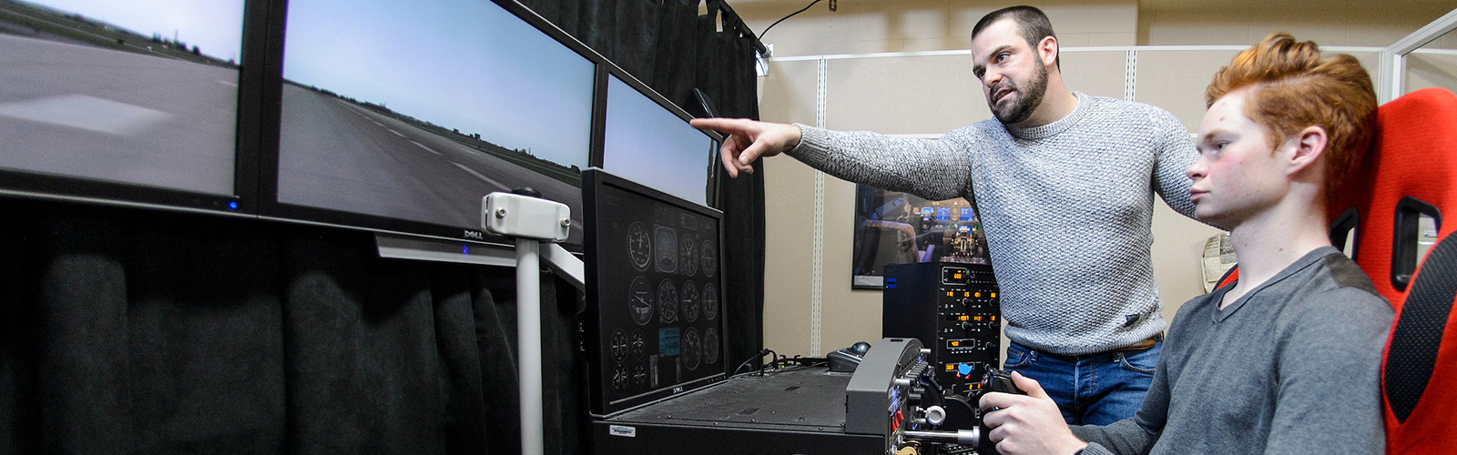 Student sits in front of flight simulator with instructor offering guidance.